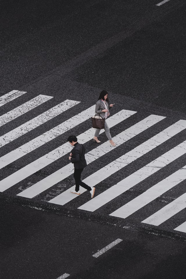 Grafika przedstawiająca dwoje ludzi przechodzących przez przejście dla pieszych.
