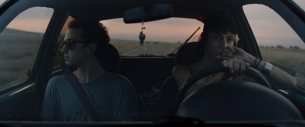 Zdjęcie przedstawiające młodych kobietę i mężczyznę podróżujących samochodem o zachodzie słońca.
