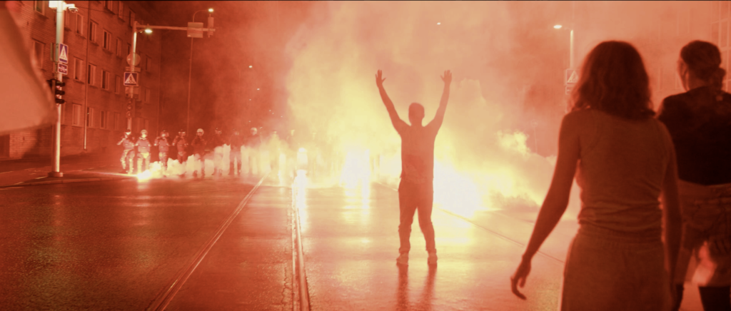 Zdjęcie przedstawiające mężczyznę stojącego z rękami w górze na ulicy podczas protestu.