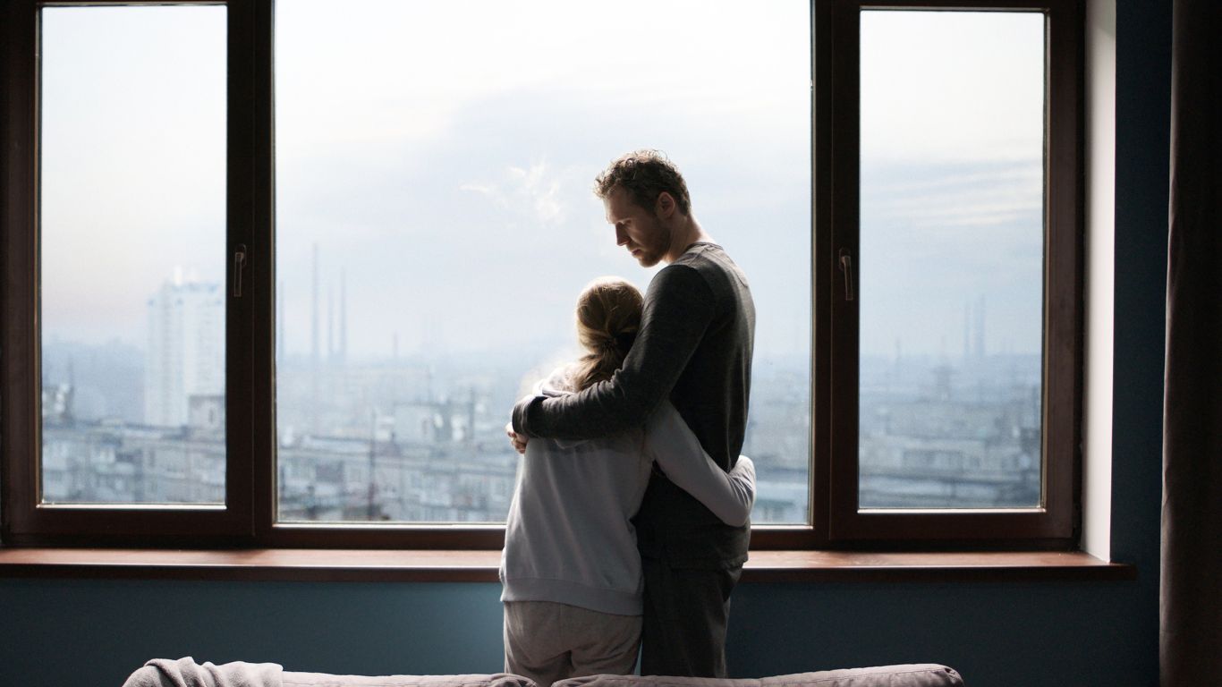 Odbicie. Zdjęcie przedstawiające córkę w ramionach ojca stojących przy oknie.