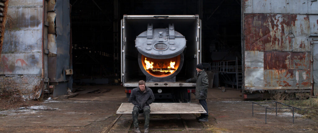 Zdjęcie przedstawiające dwóch mężczyzn przy ciężarówce, w środku której znajduje się rozpalony piec.