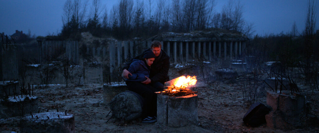 Zdjęcie przedstawiające chłopca w objęciach mężczyzny siedzących przy ognisku.